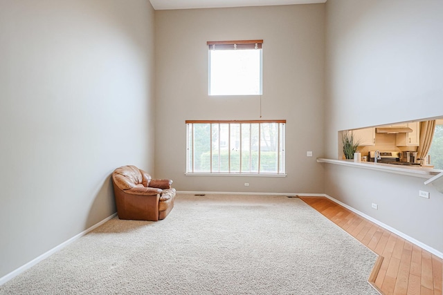 sitting room featuring a high ceiling, light wood-style floors, and baseboards