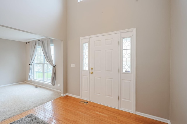 foyer entrance with visible vents, a high ceiling, light wood finished floors, and baseboards