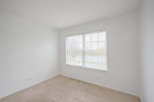empty room with carpet, visible vents, and baseboards