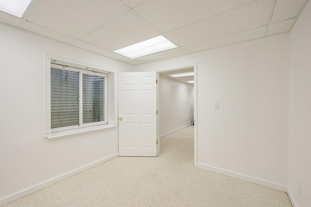 carpeted spare room featuring a drop ceiling and baseboards