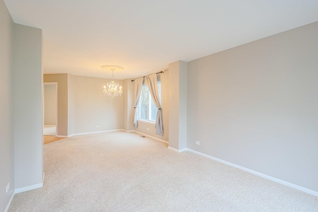 spare room with baseboards, a notable chandelier, and light carpet