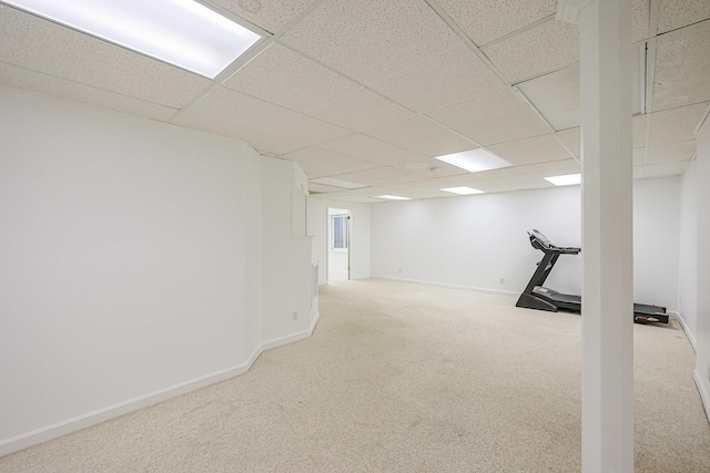 finished basement featuring a drop ceiling, light carpet, and baseboards