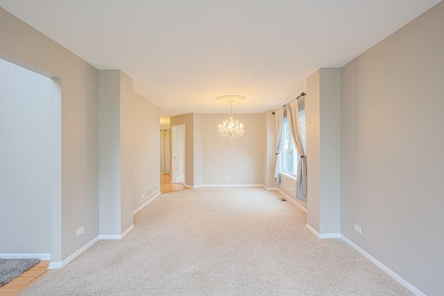 empty room featuring visible vents, a notable chandelier, light colored carpet, and baseboards
