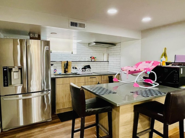 kitchen with a breakfast bar, light wood-style floors, tasteful backsplash, visible vents, and black appliances
