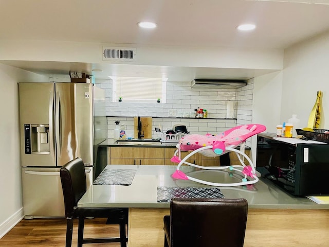 kitchen featuring black microwave, stainless steel fridge with ice dispenser, decorative backsplash, wood finished floors, and visible vents