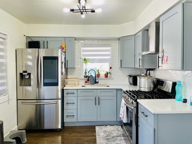 kitchen featuring wall chimney range hood, light countertops, gray cabinets, a sink, and stainless steel appliances