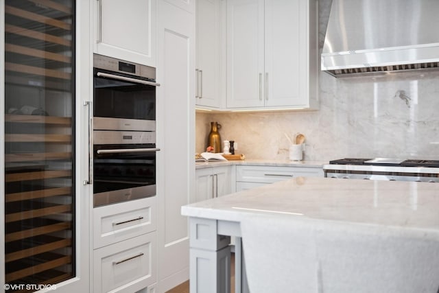 kitchen featuring white cabinets, beverage cooler, stainless steel double oven, wall chimney exhaust hood, and tasteful backsplash