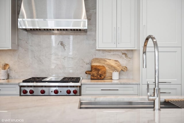 kitchen with white cabinets, a sink, tasteful backsplash, stainless steel gas stovetop, and wall chimney range hood