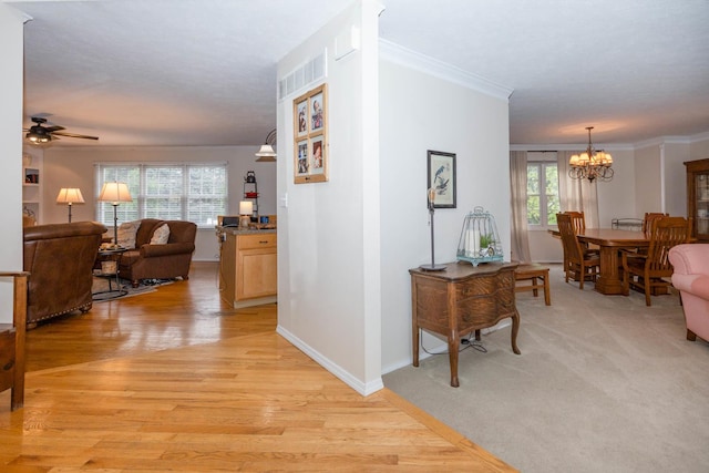 corridor featuring a notable chandelier, baseboards, ornamental molding, visible vents, and light wood-type flooring