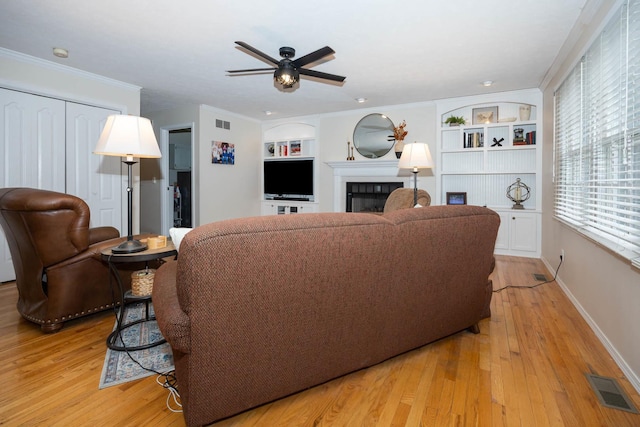 living area with light wood finished floors, a ceiling fan, a fireplace, visible vents, and built in shelves