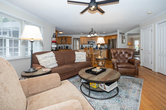 living area featuring light wood-style floors, ceiling fan with notable chandelier, and ornamental molding