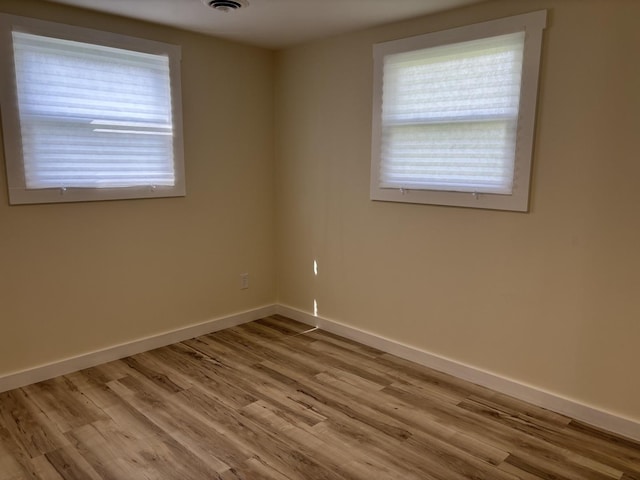 spare room with wood finished floors, visible vents, and baseboards