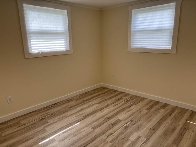 spare room featuring ornamental molding, light wood-style flooring, and baseboards