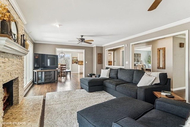 living room featuring crown molding, a stone fireplace, a ceiling fan, baseboards, and wood finished floors