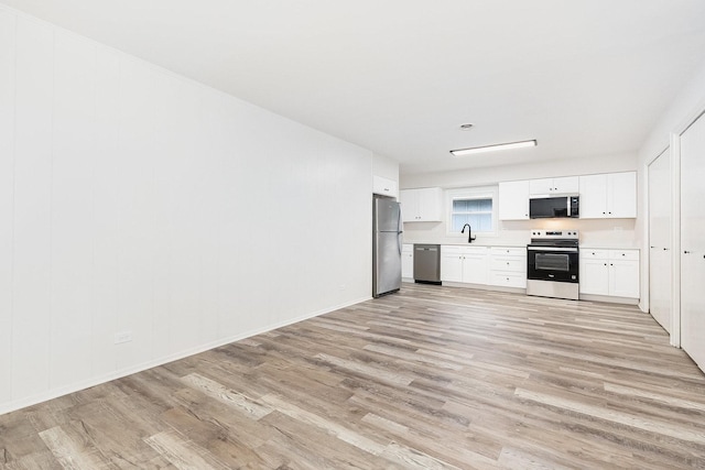kitchen with a sink, light wood finished floors, light countertops, white cabinets, and appliances with stainless steel finishes