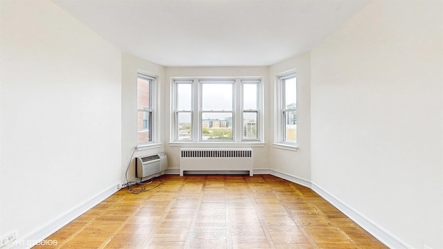 spare room featuring light wood-style flooring, baseboards, a wall mounted AC, and radiator heating unit