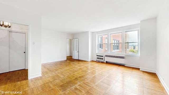 empty room with baseboards, a notable chandelier, radiator heating unit, and light wood-type flooring