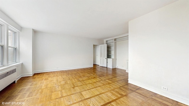 unfurnished bedroom with light wood finished floors, baseboards, and radiator heating unit