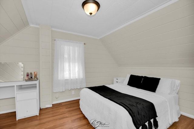 bedroom featuring lofted ceiling, baseboards, wood finished floors, and ornamental molding