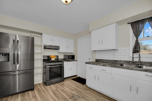 kitchen with dark countertops, a sink, appliances with stainless steel finishes, white cabinets, and under cabinet range hood