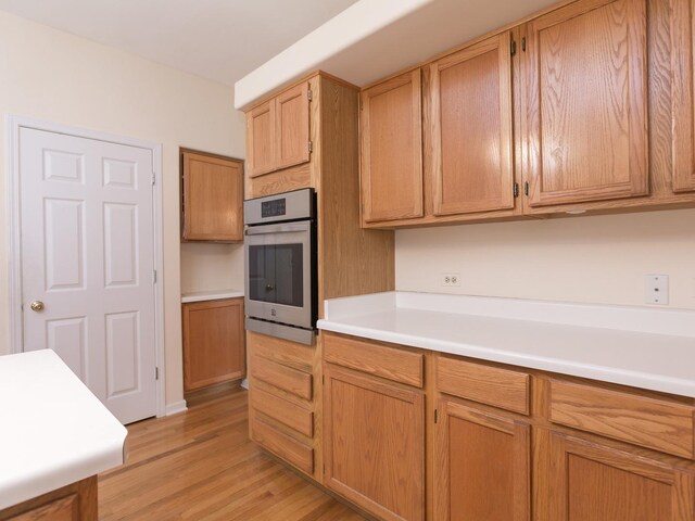 kitchen featuring stainless steel oven, light wood-style floors, and light countertops