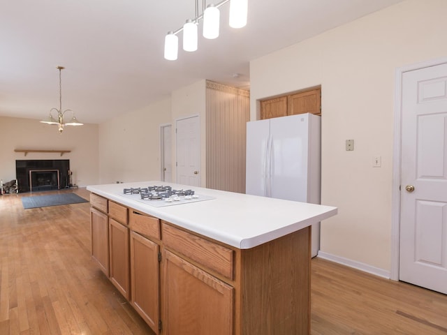 kitchen with a center island, light wood-style floors, white appliances, a fireplace, and decorative light fixtures