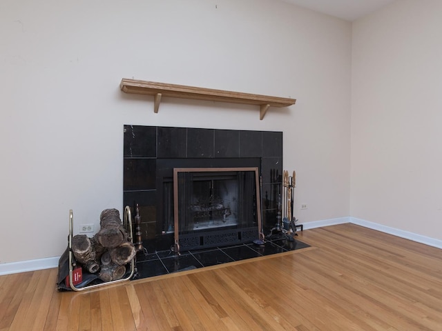 room details featuring baseboards, wood finished floors, and a tiled fireplace