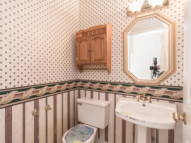 half bath with wallpapered walls, a sink, and toilet
