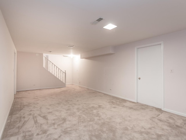 finished below grade area with baseboards, visible vents, stairs, and light carpet