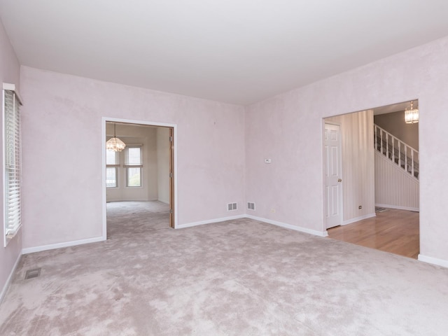 carpeted empty room featuring baseboards, visible vents, an inviting chandelier, and stairway