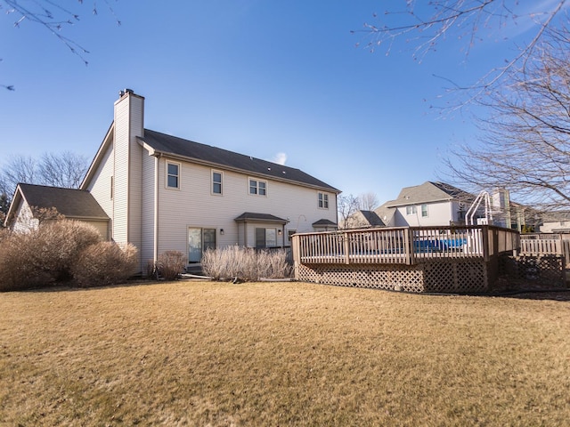 back of property with a chimney, a yard, and a deck