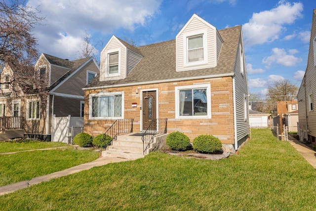 new england style home with a front lawn, stone siding, a shingled roof, and fence