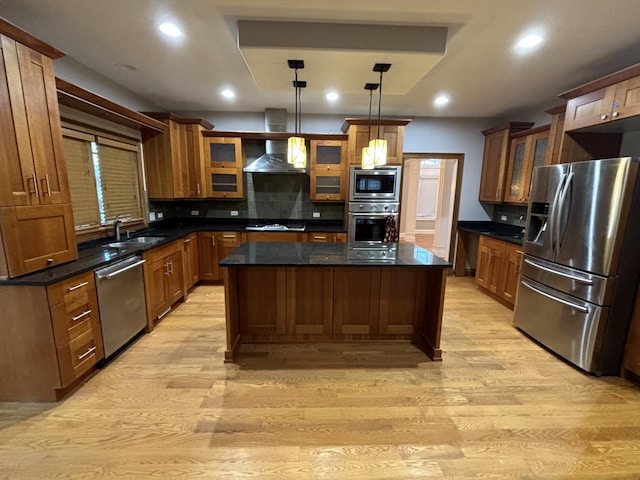 kitchen with light wood finished floors, stainless steel appliances, dark countertops, wall chimney range hood, and a center island