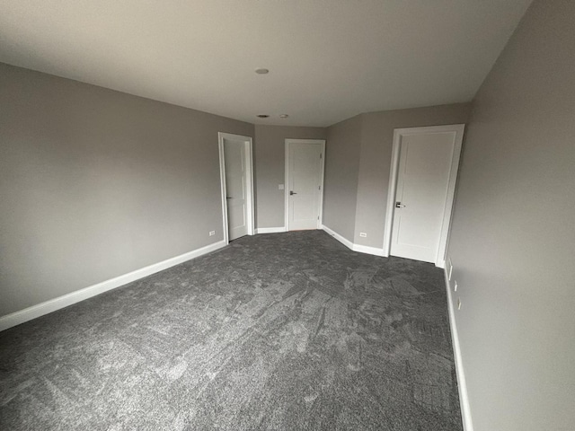 unfurnished bedroom featuring dark colored carpet and baseboards