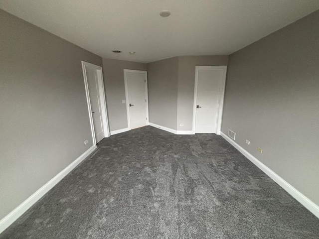 unfurnished bedroom featuring baseboards, visible vents, and dark carpet