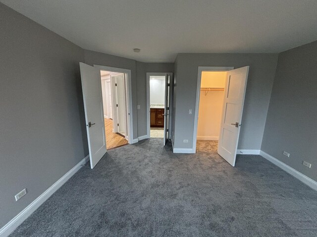 unfurnished bedroom featuring dark colored carpet, baseboards, a spacious closet, and a closet