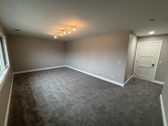 spare room featuring dark carpet, visible vents, baseboards, and track lighting