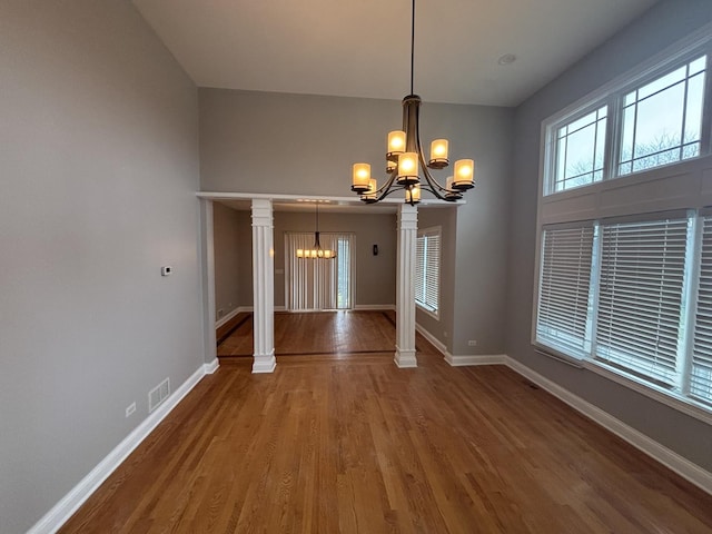 unfurnished dining area with visible vents, baseboards, wood finished floors, and an inviting chandelier