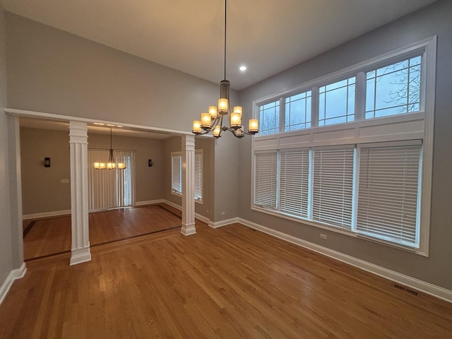 unfurnished dining area featuring a chandelier, wood finished floors, ornate columns, and baseboards