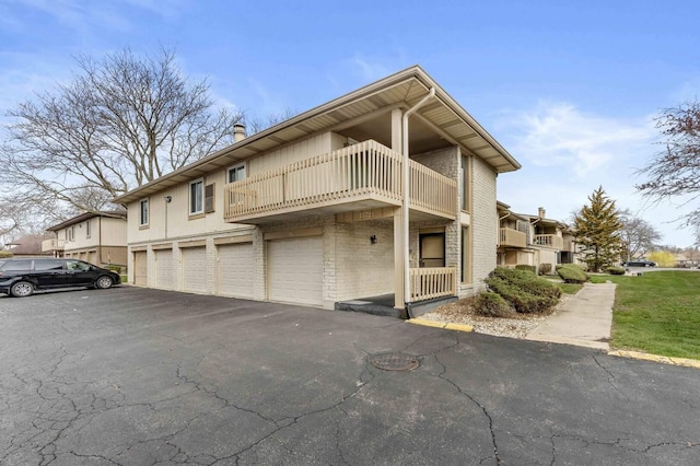 view of side of property with an attached garage, brick siding, a balcony, and driveway