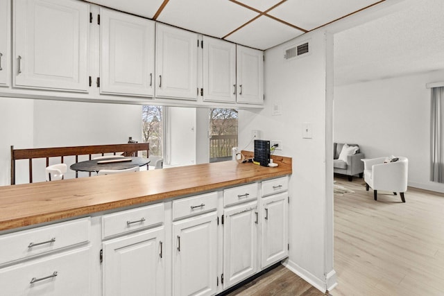 kitchen featuring white cabinets, baseboards, wood finished floors, and visible vents