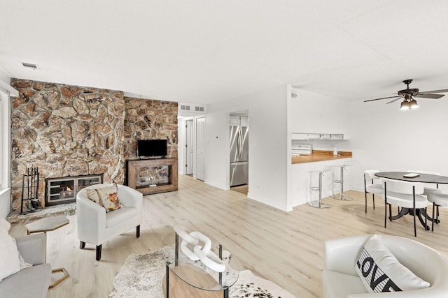 living room featuring light wood finished floors, visible vents, a fireplace, and ceiling fan