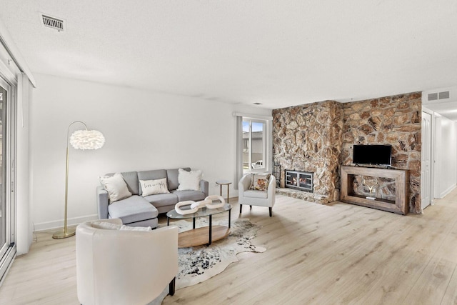 living room featuring a stone fireplace, visible vents, baseboards, and light wood-type flooring