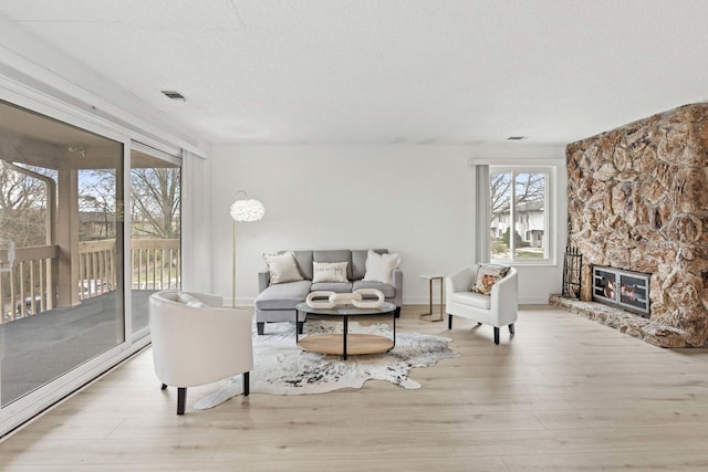 living room with wood finished floors, visible vents, baseboards, and a stone fireplace
