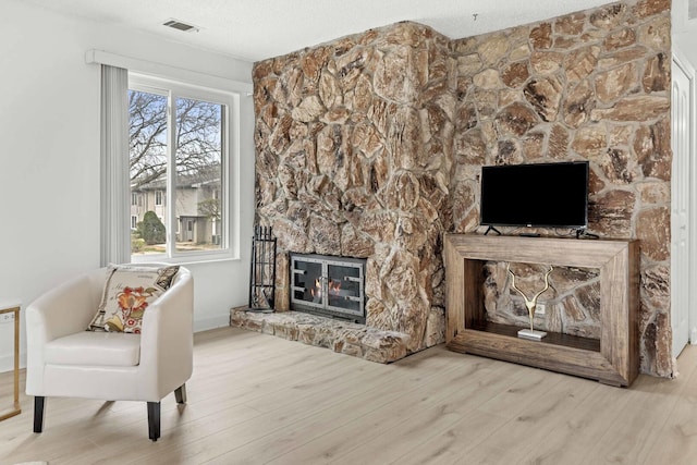 unfurnished living room with visible vents, wood finished floors, and a stone fireplace