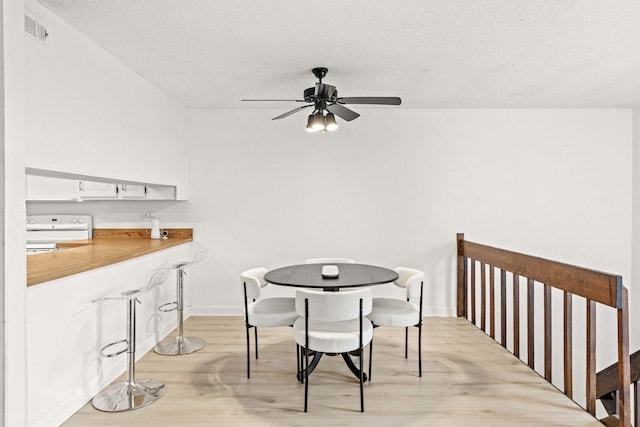 dining area featuring light wood finished floors, a ceiling fan, visible vents, and a textured ceiling