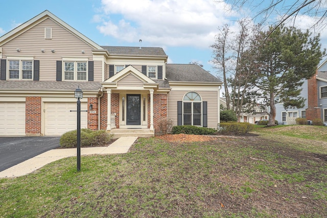 traditional-style house featuring brick siding, aphalt driveway, a front yard, and a garage