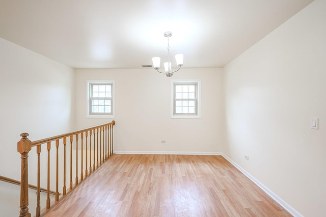 unfurnished room featuring light wood-style flooring, a wealth of natural light, and an inviting chandelier