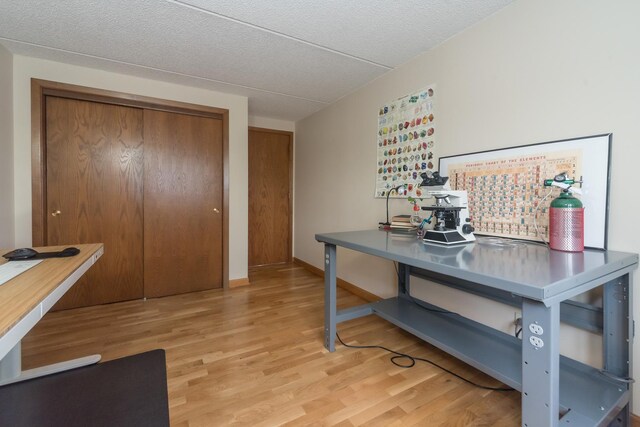 home office featuring light wood-style floors, baseboards, and a textured ceiling