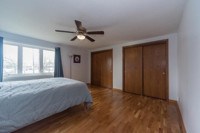 bedroom featuring multiple closets, baseboards, a ceiling fan, and wood finished floors